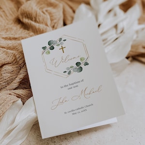 Puede incluir: Una tarjeta blanca con un marco geométrico dorado y hojas verdes. El texto dice "Bienvenido al bautismo de nuestro hijo John Michael Iglesia Católica Santa Cecilia 23 de mayo de 20XX".