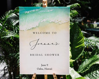 Peut inclure: Une pancarte blanche avec une scène de plage en haut et le texte "Bienvenue au Bridal Shower de Joanna le 9 juin à Oahu, Hawaï" sur un chevalet en bois.