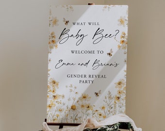 May include: A rectangular sign on an easel featuring yellow wildflower illustrations and bees. The text reads: WHAT WILL Baby Bee? WELCOME TO Emma and Brian's GENDER REVEAL PARTY. The sign is decorated with a draped beige fabric and green foliage.