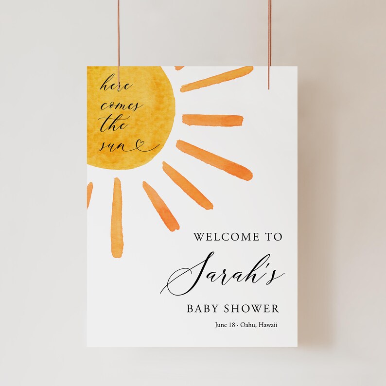 May include: A white welcome sign with a watercolor illustration of a yellow sun with orange rays. The text "here comes the sun" is written in black cursive script. The text "Welcome to Sarah's Baby Shower June 18 - Oahu, Hawaii" is written in black.