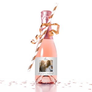 Peut inclure: Une petite bouteille de champagne ros&eacute; avec un ruban dor&eacute; et une paille ray&eacute;e. La bouteille porte une &eacute;tiquette avec une photo de deux femmes et le texte "Ellie, veux-tu &ecirc;tre ma demoiselle d'honneur ?"