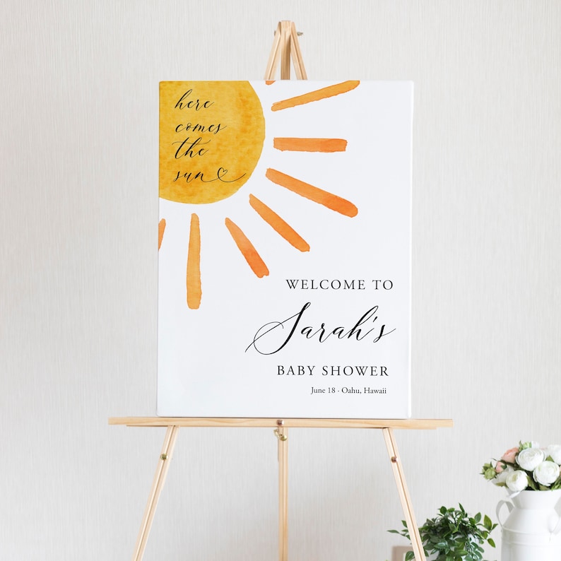 May include: Welcome to Sarah's Baby Shower sign with a watercolor sun illustration and the text "here comes the sun" in black cursive. The sign also includes the date and location of the event: June 18 - Oahu, Hawaii.