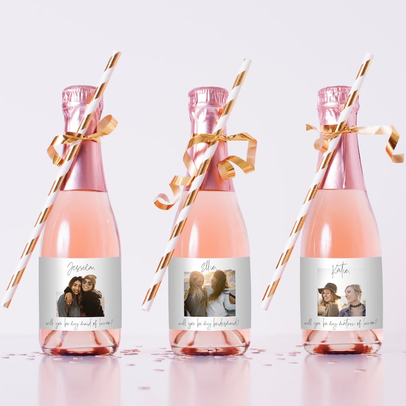 Peut inclure: Trois mini-bouteilles de champagne avec des &eacute;tiquettes personnalis&eacute;es comportant des photos et le texte "will you be my..." Les &eacute;tiquettes sont blanches avec une bordure grise et un fond de paillettes dor&eacute;es. Chaque bouteille est munie d'une paille ray&eacute;e dor&eacute;e et blanche.