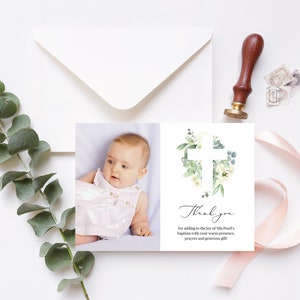 May include: Thank you card with a white cross surrounded by green leaves and white flowers. A photo of a baby girl in a white dress is on the left side of the card.