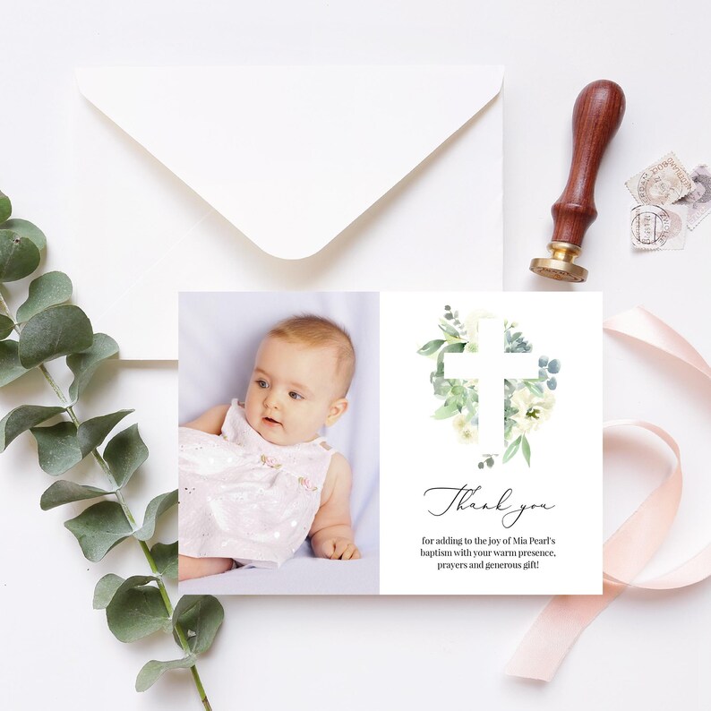 May include: Thank you card with a white cross surrounded by green leaves and white flowers. A photo of a baby girl in a white dress is on the left side of the card.