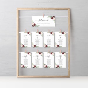 May include: A set of eight table cards with floral designs in shades of burgundy and pink. Each card has a table number and a list of names. The cards are hung on a wooden frame with clothespins. The top card reads "find your seat" with the names Michelle Lawrence & Brian Martin.