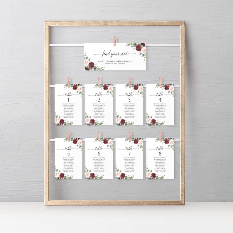 May include: A set of eight table cards with floral designs in shades of burgundy and pink. Each card has a table number and a list of names. The cards are hung on a wooden frame with clothespins. The top card reads "find your seat" with the names Michelle Lawrence & Brian Martin.