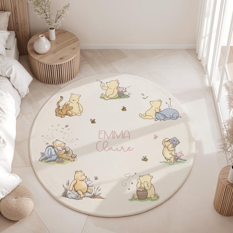 May include: A circular rug in cream, decorated with illustrations of Winnie the Pooh characters. The rug displays the names "EMMA Claire" in pink script. The design incorporates bees, butterflies, and other whimsical details, suitable for a nursery or playroom setting.