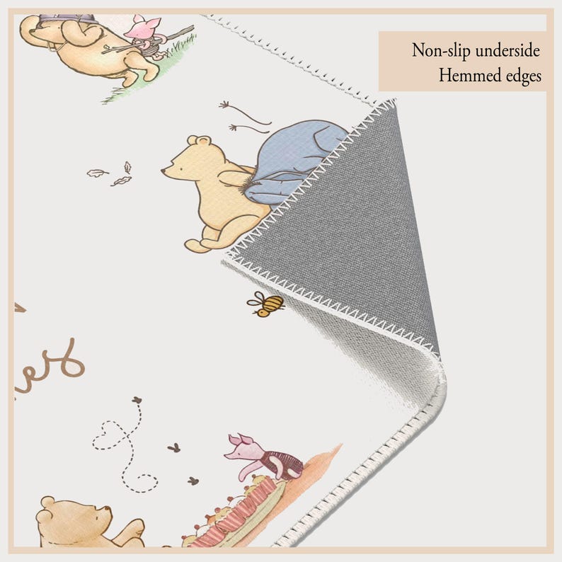 May include: A rectangular rug with illustrations of Winnie the Pooh and friends. The rug has a white background, stitched border, and a grey, non-slip underside. The image includes the text "Non-slip underside" and "Hemmed edges".