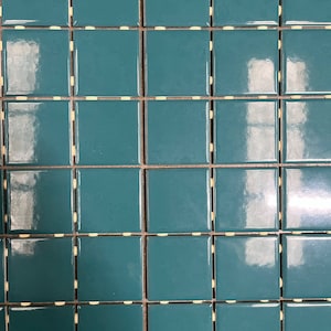 May include: Close-up of a grid of teal square tiles. Each tile is a glossy teal color with a slight sheen. The grout lines are dark gray with a thin, light-colored accent. The tiles are arranged in a neat, repeating pattern.