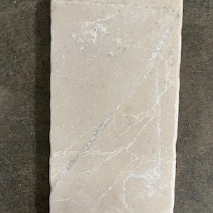 May include: A light beige rectangular tile with a white veined pattern. The tile has a rough, textured surface.