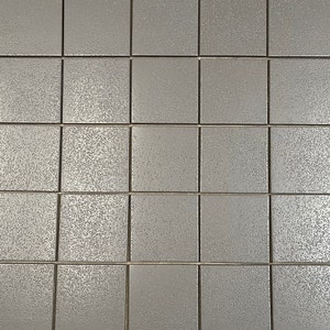May include: A close-up of a wall covered in gray square tiles. The tiles have a textured surface.