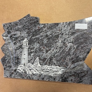May include: A gray granite headstone with a carved image of a lighthouse, a sailboat, and waves. The headstone is shaped like a wave and has the text "MP-15" on it.