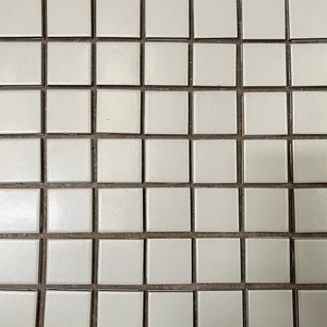 May include: A white tiled wall with black grout lines. The tiles are arranged in a grid pattern.