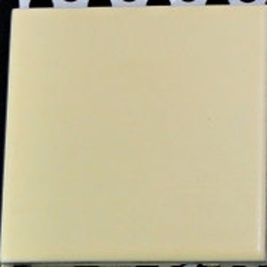 May include: A square ceramic tile in a creamy off-white color.