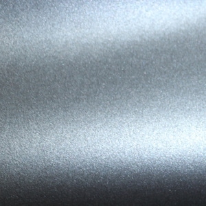 May include: A close-up of a smooth, silver-colored surface with a subtle, textured pattern. The surface reflects light, creating a shimmering effect.