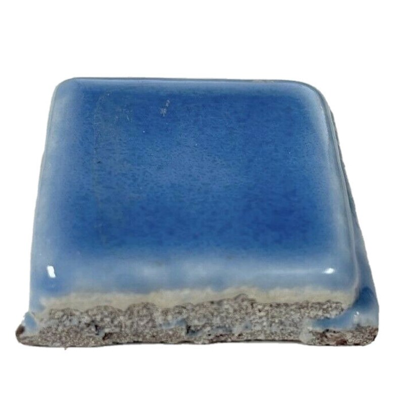 May include: A square ceramic tile with a light blue glaze. The tile has a rough, uneven edge.