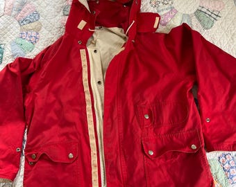 May include: A red hooded jacket with a white lining and two large pockets. The jacket has a zip closure and a button flap.