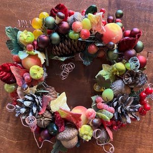 May include: A festive autumn wreath decorated with red, green, and yellow berries, pinecones, acorns, and leaves.