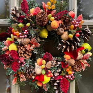 May include: A festive Christmas wreath with red velvet bows, pine branches, pinecones, and various fruits and berries. The wreath is decorated with lemons, oranges, and other seasonal accents.