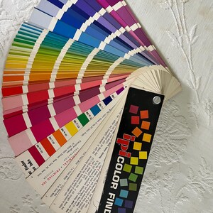 Peut inclure: Un nuancier en &eacute;ventail avec une &eacute;tiquette noire et blanche indiquant "COATED iPI COLOR FINDER". Le nuancier est ouvert pour r&eacute;v&eacute;ler une vari&eacute;t&eacute; de nuanciers de couleurs, y compris des nuances de rouge, orange, jaune, vert, bleu, violet et rose.