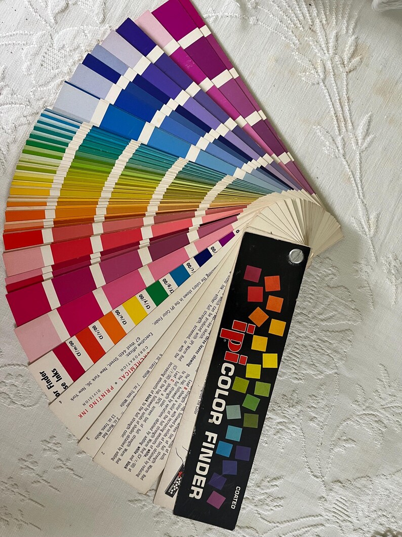 Peut inclure: Un nuancier en &eacute;ventail avec une &eacute;tiquette noire et blanche indiquant "COATED iPI COLOR FINDER". Le nuancier est ouvert pour r&eacute;v&eacute;ler une vari&eacute;t&eacute; de nuanciers de couleurs, y compris des nuances de rouge, orange, jaune, vert, bleu, violet et rose.