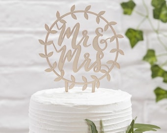 May include: A wooden cake topper with a wreath of leaves and the words "Mr & Mrs" in a cursive font.