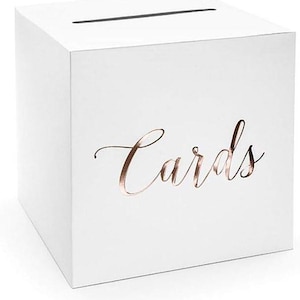 May include: A white, cube-shaped card box with a slot on top. The word "Cards" is written in elegant rose gold script on the front. Suitable for weddings, parties, or special occasions.