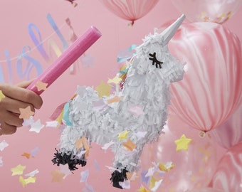 May include: A white unicorn piñata with rainbow streamers and confetti stars. The piñata is being hit with a pink stick.