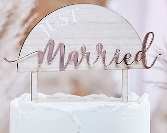 May include: A white wooden cake topper with the words "Just Married" in rose gold lettering. The topper is shaped like a half circle.