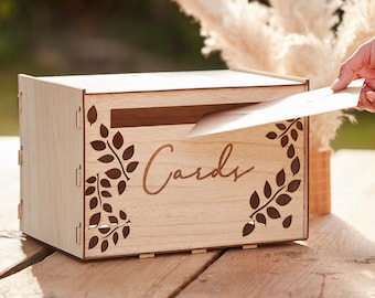 May include: A wooden card box with a slot for cards. The box has a cutout design of leaves and the word "Cards" is written on the front.