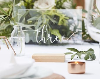 May include: Clear acrylic table number with the word "three" written in white calligraphy on a wooden base.