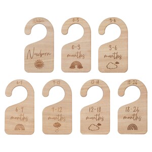 May include: Set of eight wooden hanger tags with different age ranges for baby clothes, including Newborn, 0-3 months, 3-6 months, 6-9 months, 9-12 months, 12-18 months, and 18-24 months. Each tag features a different design, including a sun, rainbow, clouds, and raindrops.