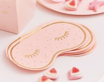May include: Pink paper sleep mask with gold eyelashes and polka dots. The mask is folded in a stack of several masks.