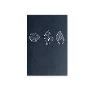 Könnte beinhalten: Ein schwarzes Notizbuch mit drei weißen Illustrationen von Muscheln. Das Notizbuch ist geschlossen und hat eine strukturierte Oberfläche.