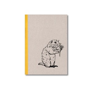 Könnte beinhalten: Ein braunes Notizbuch mit gelbem Rücken und einer Schwarzweißillustration eines Präriehundes, der eine Löwenzahnpflanze hält, auf dem Einband.