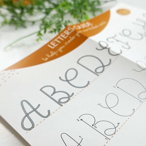 May include: A calligraphy guide showing the letters A, B, D, E, and H in a cursive style. The guide includes instructions on how to create each letter. The guide is white with grey lettering and an orange accent.