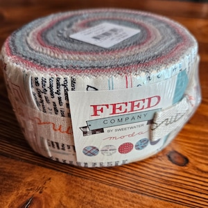 May include: A roll of fabric with a white background and colourful stripes. The fabric is labelled "FEED COMPANY BY SWEETWATER moda".