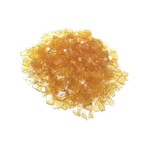 Peut inclure: Un tas de flocons de gomme-laque translucides de couleur ambre avec des bords irréguliers et dentelés. Les petits morceaux fins et cassants varient en taille et en forme, créant un aspect cristallin texturé avec une finition brillante.