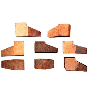Puede incluir: Siete bloques de madera individuales, cada uno con un perfil distintivo en forma de cuña o escalonado. Las piezas muestran una veta de madera natural con tonos variados de bronceado claro y marrón rojizo profundo, con textura bruta.