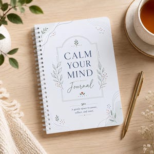 May include: A white spiral-bound journal with the text CALM YOUR MIND Journal and A gentle space to pause, reflect, and reset. The cover features a dark blue arched frame, delicate green leaf illustrations, and small red heart accents.