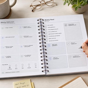 May include: A spiral-bound planner open to a two-page spread titled Weekly Reflection and Weekly Reset. The pages feature lined sections for tasks, reflections, and checklists with printed prompts like Things I completed, Check calendar, and What needs preparation.