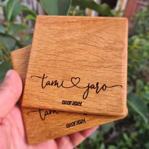 Op de afbeelding: Twee houten onderzetters met de gegraveerde namen "Tami" en "Jaro", samen met een hartje en de datum "02.07.2021".