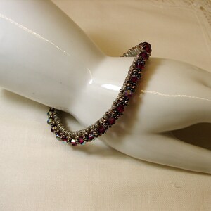 May include: A close-up of a red and gold beaded bracelet on a white mannequin hand. The bracelet is made of small, round beads and has a spiral design.