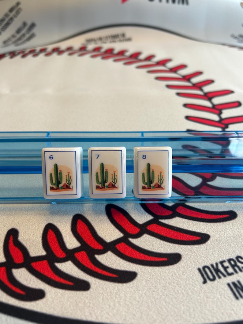 May include: Three white game tiles with the numbers 6, 7, and 8. Each tile features a desert scene with a cactus and a setting sun. The tiles are set against a blue background, with a baseball-themed surface.