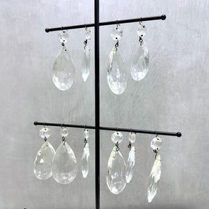 May include: A set of eight clear glass teardrop-shaped crystal prisms hanging from a black metal stand. The prisms are arranged in two rows of four.