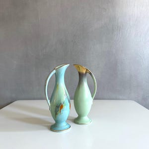Könnte beinhalten: Zwei kleine Keramikvasen mit blauer und grüner Glasur. Die Vasen haben einen goldenen Rand und eine einzigartige Form.