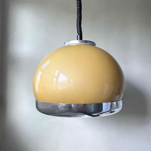 May include: A retro pendant light with a rounded, yellow-tinted glass shade. The shade is framed by a polished chrome band. A black, coiled cable suspends the light. This vintage light fixture is suitable for interior lighting, a classic design.