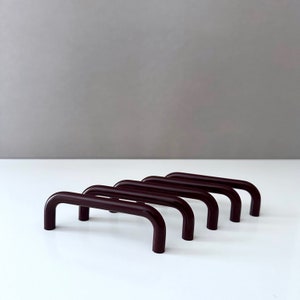 Puede incluir: Cinco tiradores o pomos de armario de color marrón oscuro en fila. Los tiradores están hechos de un material liso y brillante y tienen un diseño simple y redondeado.