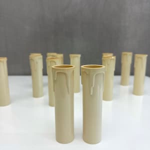 May include: A group of off-white pillar candles, some with a dripped wax effect, arranged on a white surface.